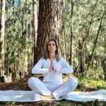 A woman sitting in the middle of a forest doing yoga
